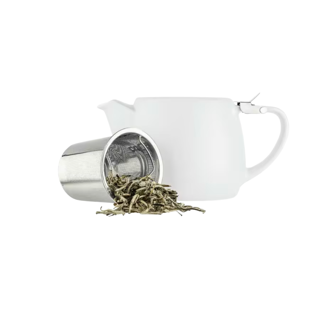 White teapot with tea infuser and loose tea leaves on a white background