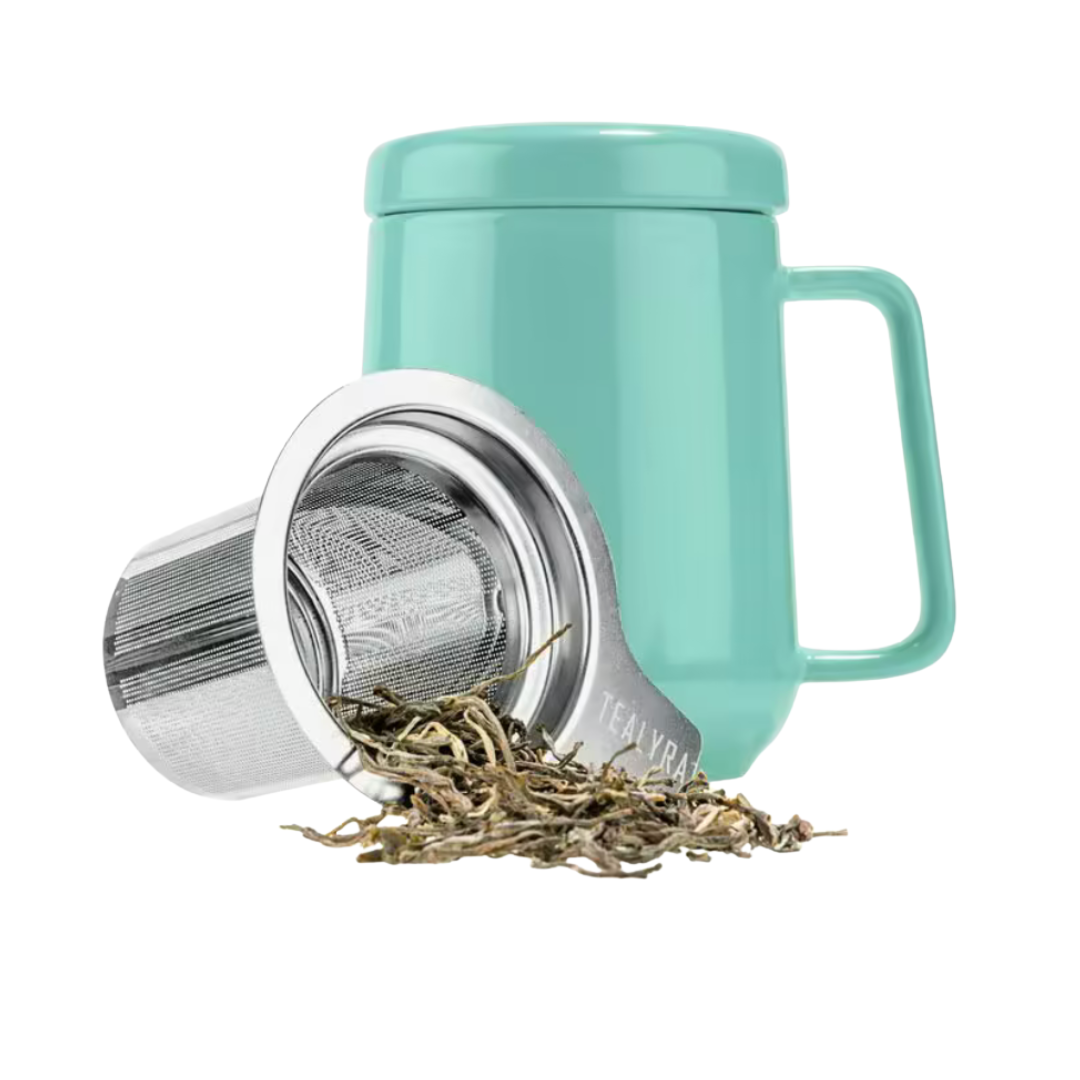 Turquoise mug with tea infuser and loose tea leaves on a white background